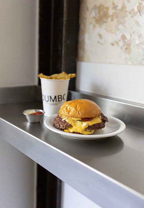 Le Cheeseburger, de chez Dumbo avec un smash patty de 130 g, une tranche d’American cheese, poivre du moulin, oignons crus émincés, salade iceberg émincée, pickles maison et sauce maison