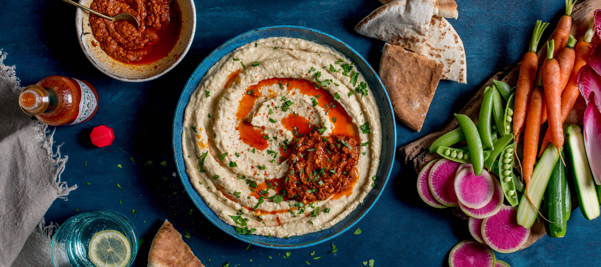 Houmous a l'harissa avec de la sauce Tabasco rouge et comme accompagnements des legumes et du pain