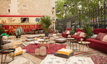 Ephemeral terrace of the Gyspy café with Emmanuelle wicker armchair, banquettes, mix and match of burlap carpets, comfy cushions, knit poufs, tropical plants at the Cirque d'Hiver in Paris