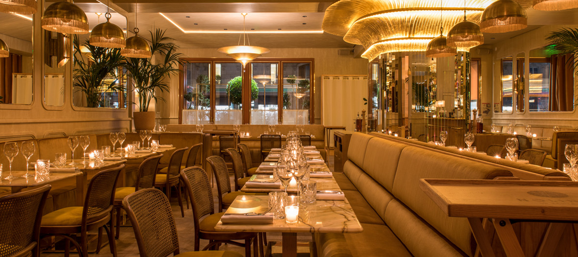 Decoration of the dining room of the Nolinski hotel with rattan chairs, marble tables, chandeliers, tropical plants and mural