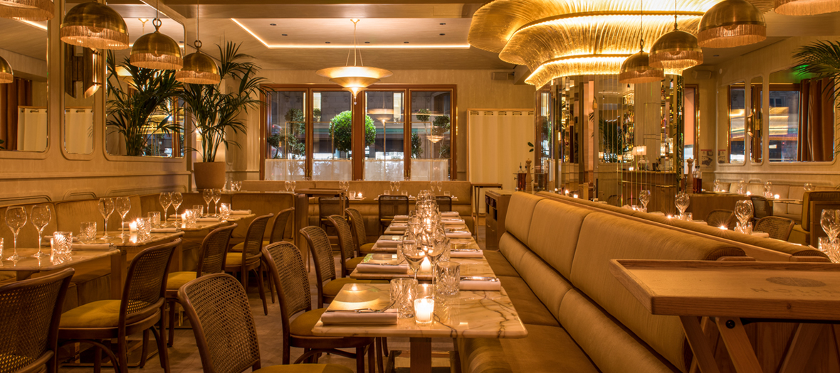 Décoration de la salle du restaurant de l’hôtel Nolinski avec chaises en rotin, tables en marbre, chandeliers, plantes tropicales et fresque murale