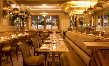 Decoration of the dining room of the Nolinski hotel with rattan chairs, marble tables, chandeliers, tropical plants and mural