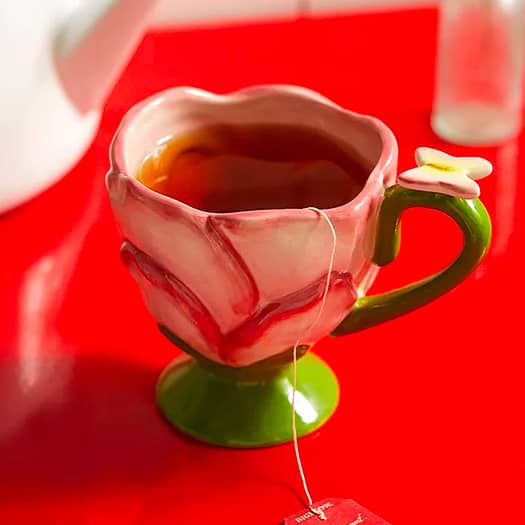 Tasse de thé rose en forme de fleur avec sachet de thé rouge, sur fond rouge vif