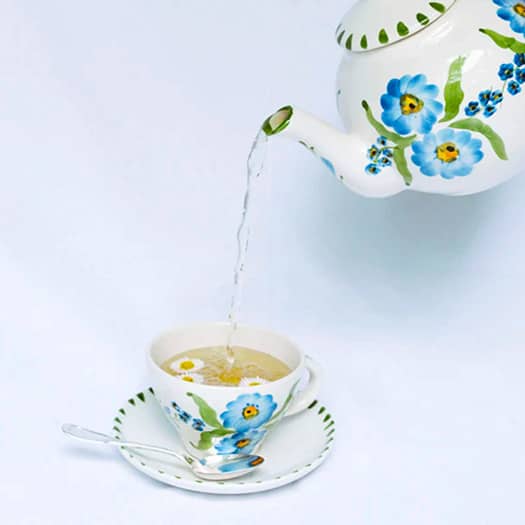 Théière blanche avec fleurs bleues, versant une infusion dans une tasse assortie