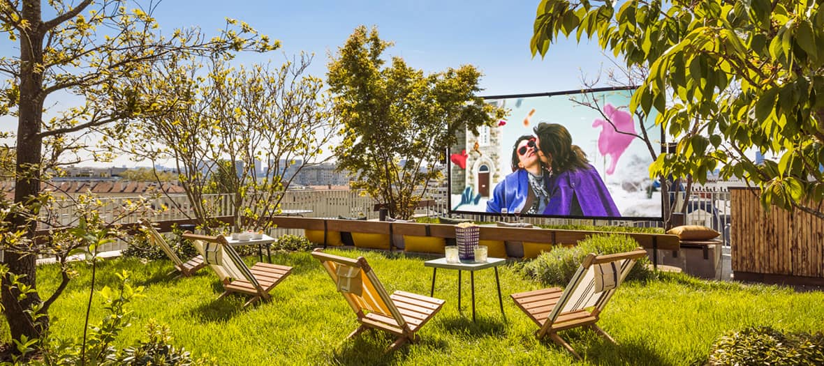 Ciné en plein air dans la cour du Louvre à la tombée de la nuit, avec spectateurs installés en transats.